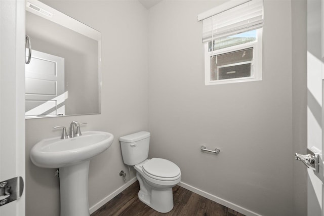 half bath with visible vents, toilet, a sink, wood finished floors, and baseboards