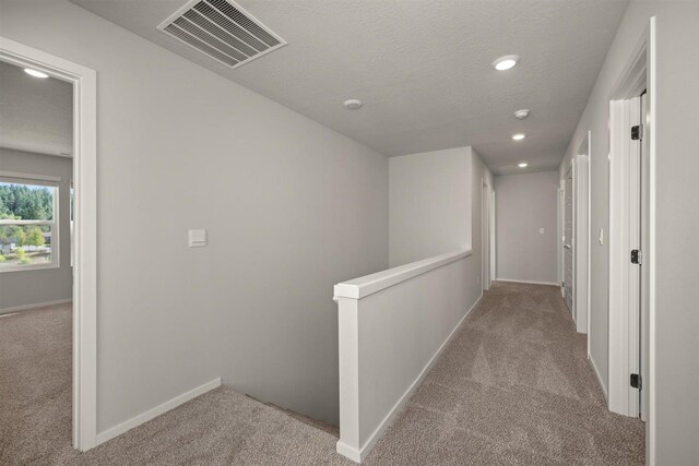 hall with light colored carpet, visible vents, a textured ceiling, an upstairs landing, and baseboards