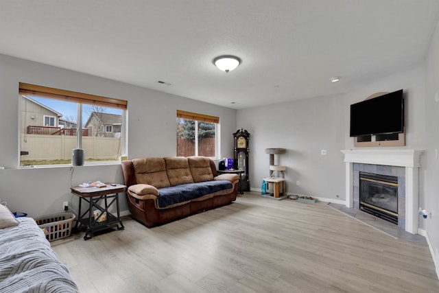 living area with baseboards, a tiled fireplace, visible vents, and light wood-style floors