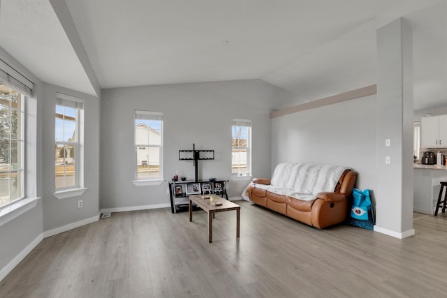 living room featuring lofted ceiling, light wood-style flooring, and baseboards