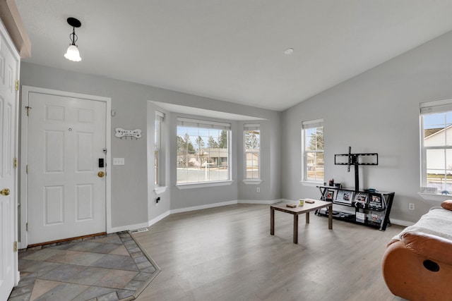 foyer entrance featuring vaulted ceiling, baseboards, wood finished floors, and a healthy amount of sunlight