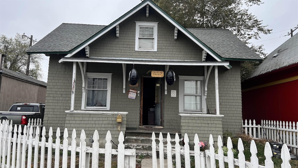 bungalow featuring covered porch, a shingled roof, and a fenced front yard