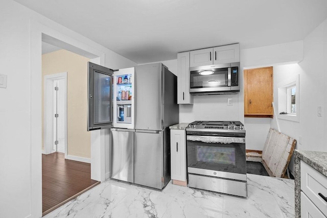 kitchen featuring stainless steel appliances, marble finish floor, white cabinets, and baseboards