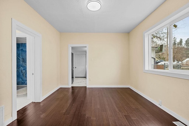 empty room featuring visible vents, baseboards, and dark wood finished floors