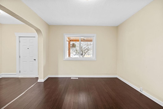 spare room with arched walkways, baseboards, and wood finished floors