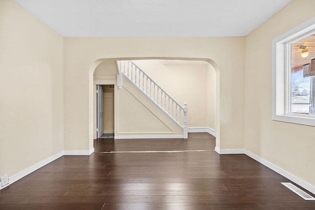 empty room featuring baseboards, visible vents, arched walkways, and wood finished floors