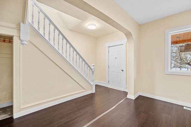 foyer entrance with arched walkways, wood finished floors, stairs, and baseboards