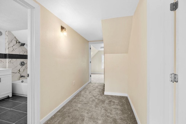 hall featuring vaulted ceiling, baseboards, and dark colored carpet