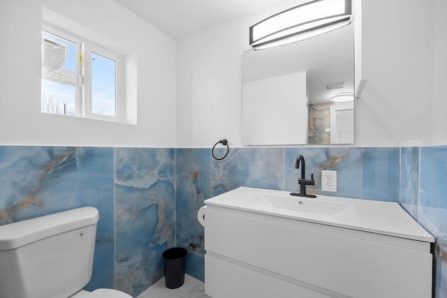 half bath with vanity, toilet, and tile walls