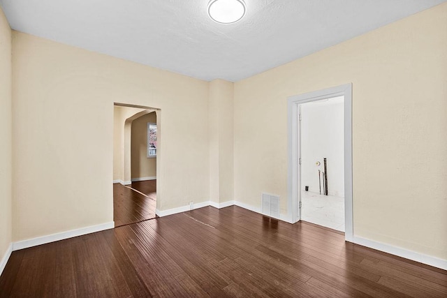 empty room with arched walkways, visible vents, hardwood / wood-style flooring, and baseboards