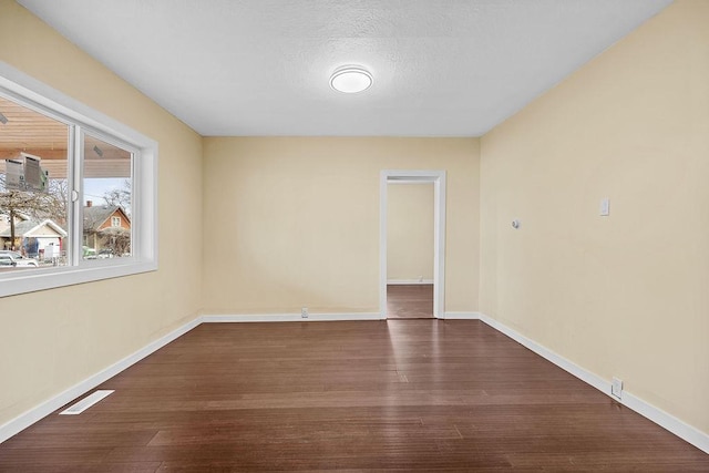 unfurnished room with a textured ceiling, dark wood-type flooring, visible vents, and baseboards