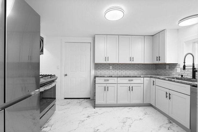 kitchen with appliances with stainless steel finishes, marble finish floor, a sink, and decorative backsplash