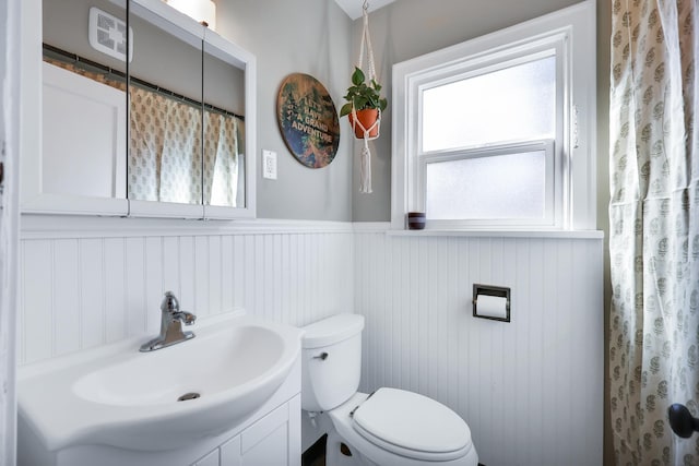 bathroom with a wainscoted wall, plenty of natural light, vanity, and toilet