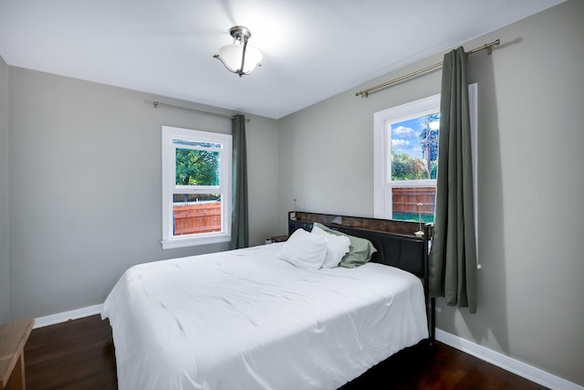 bedroom with dark wood-style floors, multiple windows, and baseboards