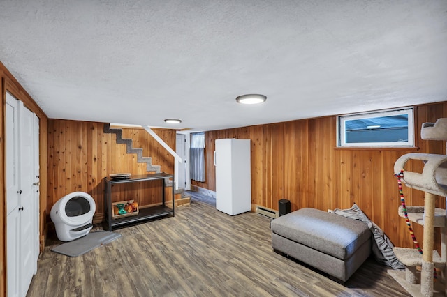 living area with wooden walls, wood finished floors, stairs, baseboard heating, and a textured ceiling