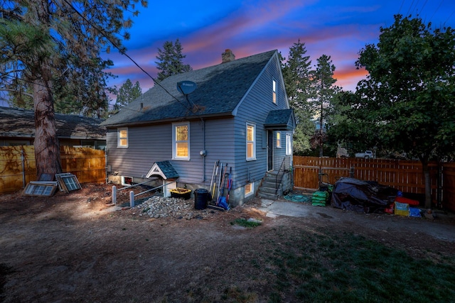 back of house at dusk featuring roof with shingles, fence, and a chimney