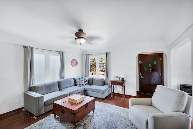 living room featuring baseboards, arched walkways, ceiling fan, and dark wood-style flooring