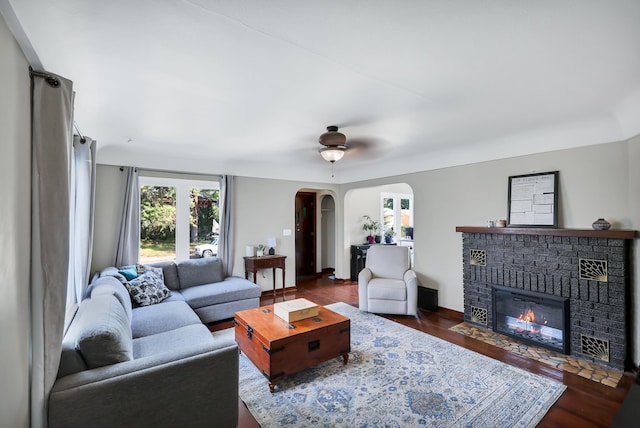 living area featuring arched walkways, a fireplace, and dark wood-style floors