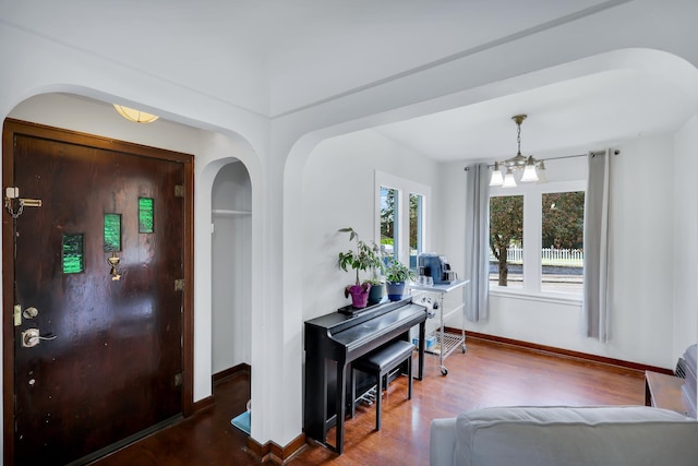 entryway with a notable chandelier, baseboards, arched walkways, and wood finished floors