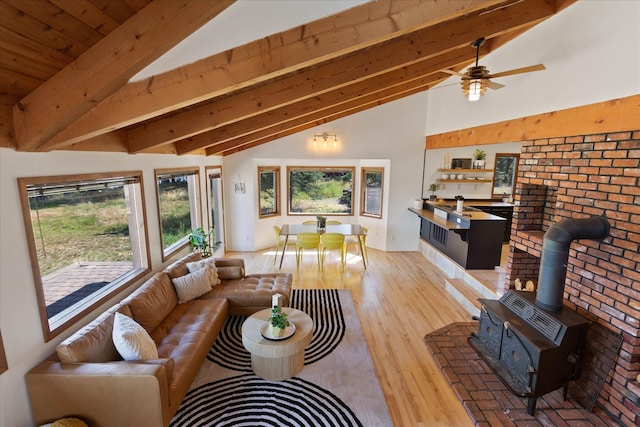 living area featuring vaulted ceiling with beams, ceiling fan, light wood-style flooring, and a wood stove