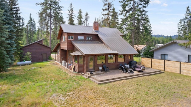 back of house featuring metal roof, fence, a yard, a wooden deck, and a chimney