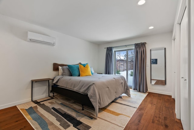 bedroom featuring an AC wall unit, wood finished floors, and baseboards