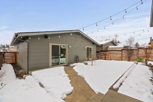 snow covered house featuring a fenced backyard