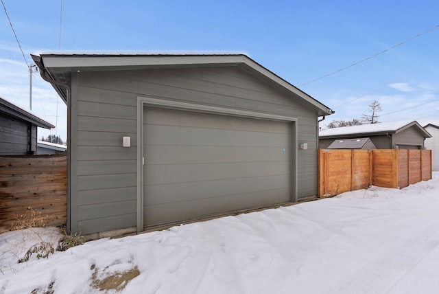 snow covered garage with a garage and fence