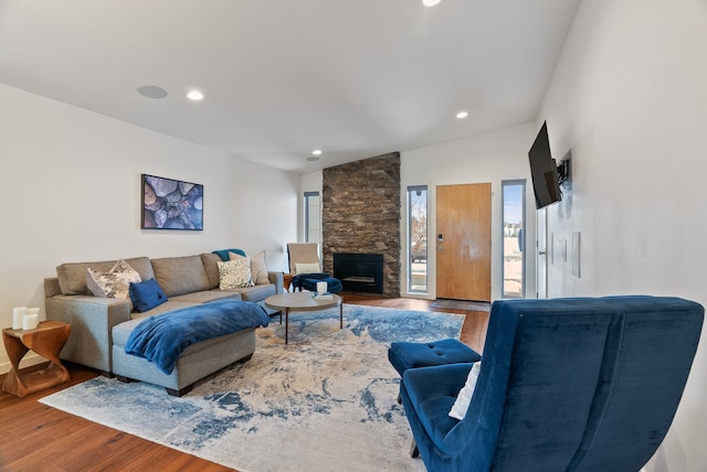 living room with a wealth of natural light, recessed lighting, wood finished floors, and a stone fireplace