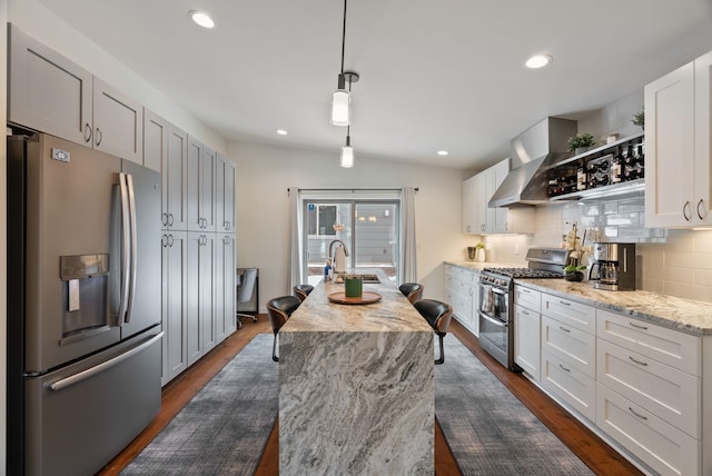 kitchen with a sink, wall chimney range hood, appliances with stainless steel finishes, backsplash, and dark wood-style floors