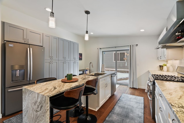 kitchen featuring wall chimney exhaust hood, appliances with stainless steel finishes, a kitchen breakfast bar, dark wood-style flooring, and a sink