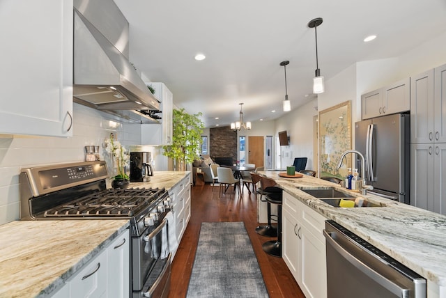 kitchen with white cabinets, appliances with stainless steel finishes, wall chimney range hood, and a sink