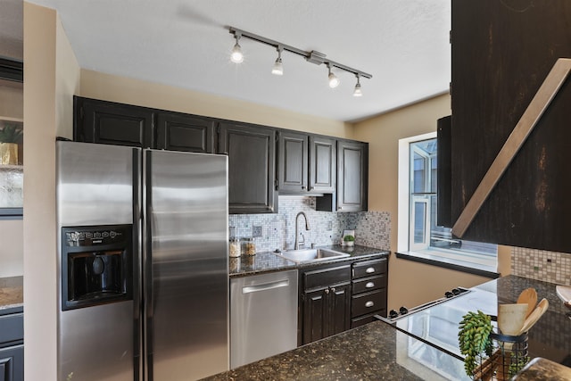 kitchen featuring dark stone counters, a sink, stainless steel appliances, dark cabinetry, and backsplash