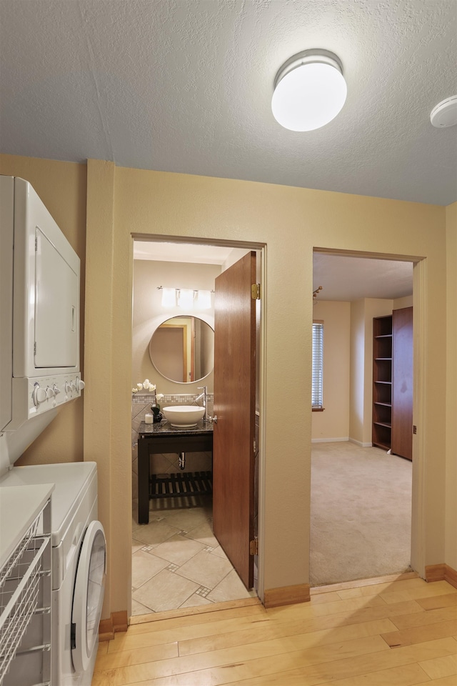 hall featuring a textured ceiling, stacked washer and dryer, a sink, and light wood-style flooring