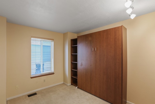 unfurnished bedroom with light carpet, baseboards, visible vents, a textured ceiling, and a closet