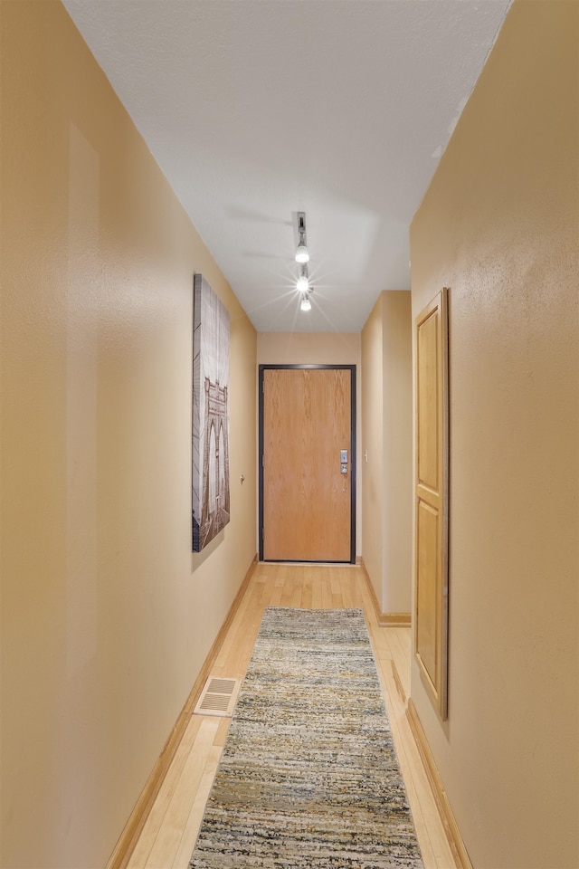 hallway featuring visible vents, light wood-style flooring, and baseboards