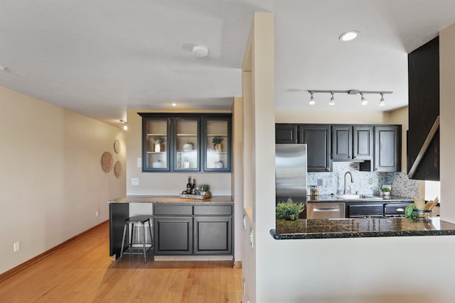 kitchen featuring tasteful backsplash, light wood-style flooring, appliances with stainless steel finishes, a sink, and baseboards