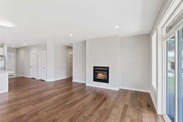 unfurnished living room featuring dark wood-style floors, recessed lighting, visible vents, a glass covered fireplace, and baseboards