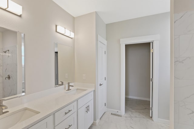 full bath with double vanity, marble finish floor, a tile shower, and a sink