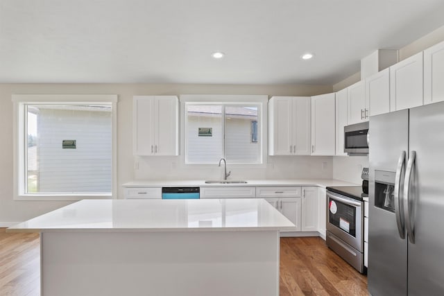 kitchen featuring light wood finished floors, appliances with stainless steel finishes, a sink, and white cabinets