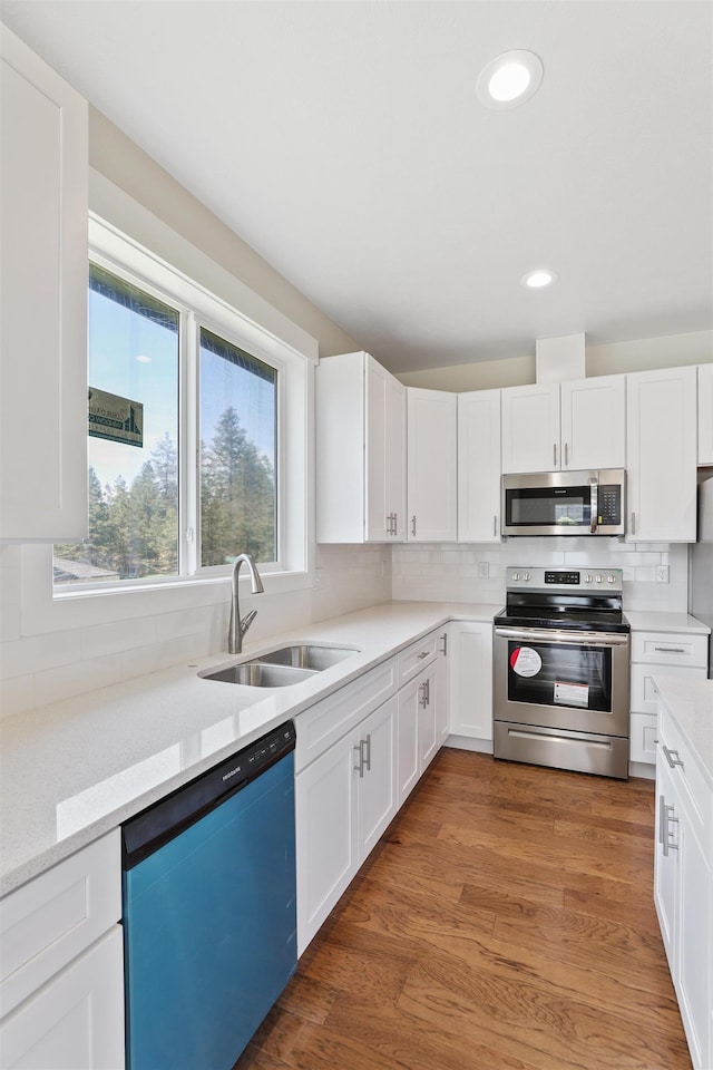 kitchen with appliances with stainless steel finishes, a sink, backsplash, and light wood-style flooring