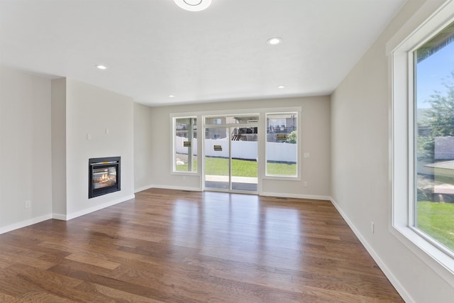 unfurnished living room with dark wood-style floors, a glass covered fireplace, baseboards, and recessed lighting