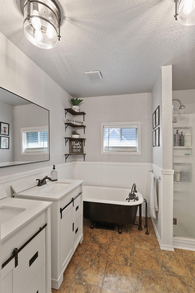 bathroom with a wainscoted wall, two vanities, a sink, a shower stall, and a textured ceiling