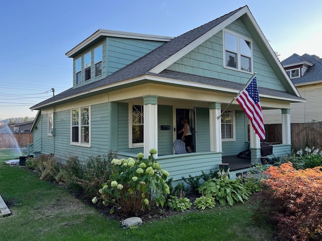 bungalow-style house featuring a porch, roof with shingles, and fence