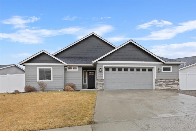 view of front of property with an attached garage, a front yard, fence, stone siding, and driveway