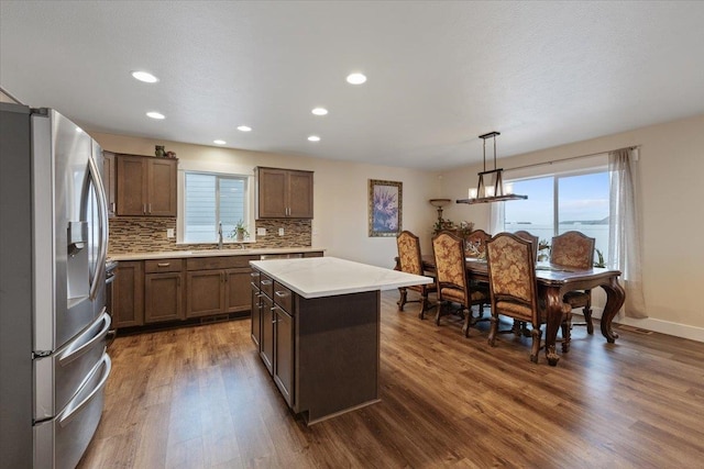 kitchen featuring dark wood-style flooring, light countertops, decorative backsplash, a kitchen island, and stainless steel fridge with ice dispenser