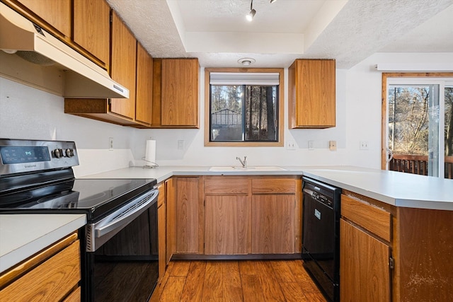 kitchen with under cabinet range hood, a peninsula, a sink, dishwasher, and stainless steel range with electric stovetop