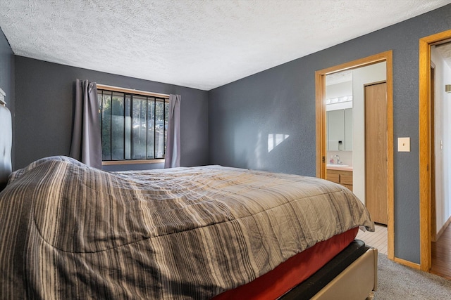 carpeted bedroom featuring ensuite bath, a textured ceiling, and a sink