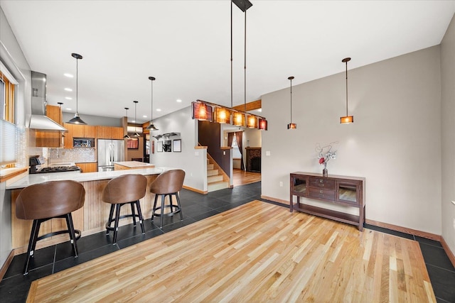 kitchen with stainless steel appliances, dark wood-style flooring, light countertops, wall chimney range hood, and tasteful backsplash