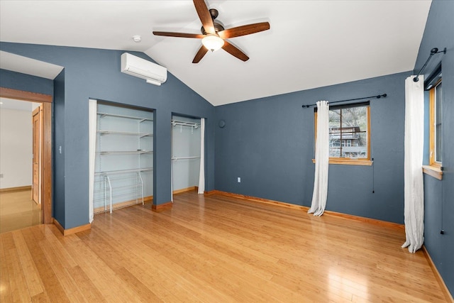 unfurnished bedroom with lofted ceiling, a wall unit AC, baseboards, light wood-type flooring, and two closets